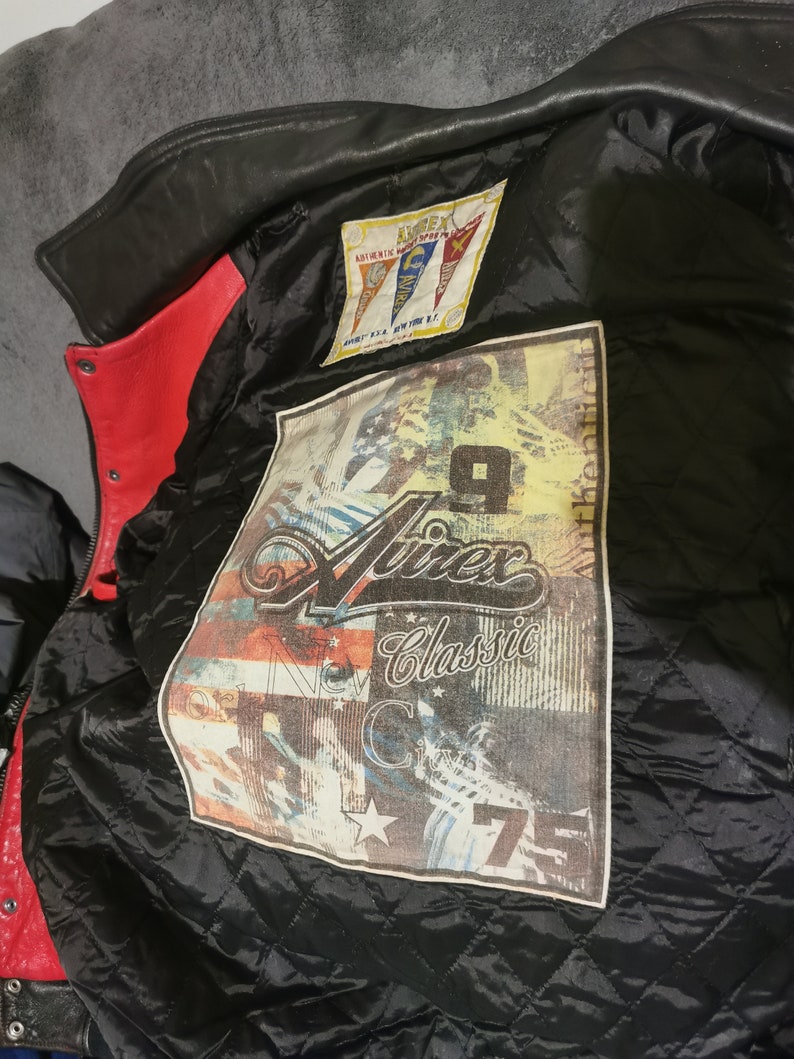 May include: A black leather jacket with a red lining. The jacket has a patch on the inside with the text "Ninex Classic" and a graphic of a motorcycle. The patch also has the text "New York City" and a star.