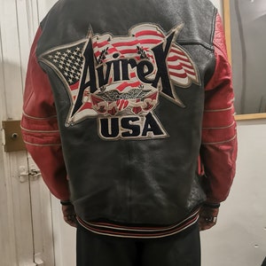 May include: A black leather jacket with red sleeves and a large embroidered patch on the back that says "Avirex USA" with an American flag design.