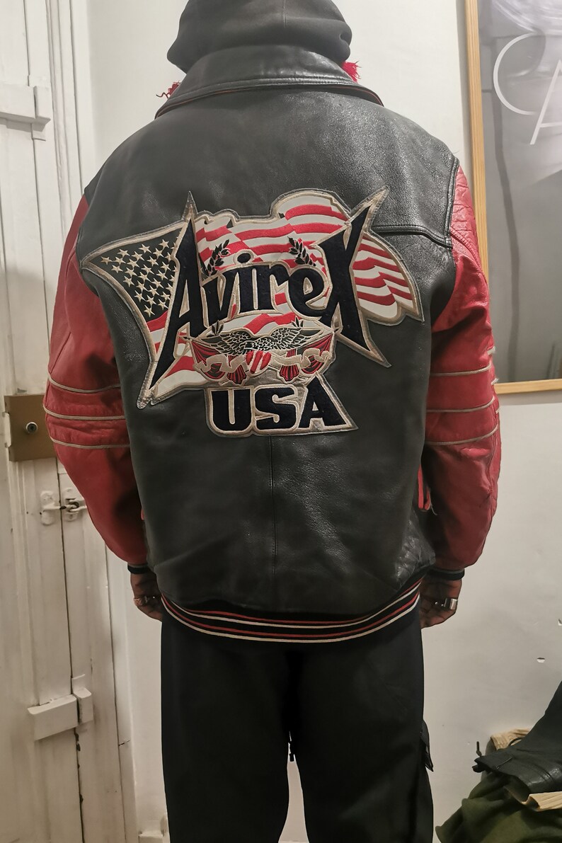 May include: A black leather jacket with red sleeves and a large embroidered patch on the back that says "Avirex USA" with an American flag design.