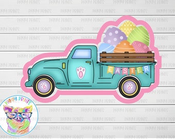 May include: A teal blue pickup truck with a wooden bed filled with pastel Easter eggs. The truck has a paw print on the side and a banner that says "EASTER".