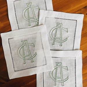 May include: Four white linen napkins with a green embroidered monogram of the letter "A" on each.