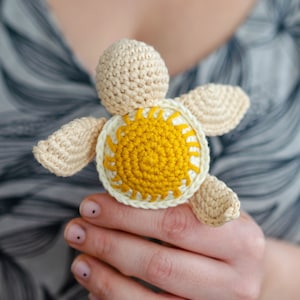 May include: A crocheted turtle toy with a yellow sun design on its shell. The turtle is made with white and yellow yarn.
