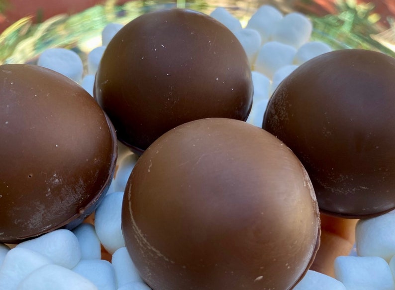 Peut inclure: Quatre boules de guimauve enrob&eacute;es de chocolat, &eacute;galement appel&eacute;es guimauves enrob&eacute;es de chocolat, sont dispos&eacute;es sur un lit de guimauves blanches.