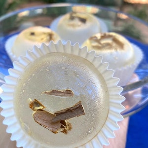 May include: Close-up of a clear, round candy with gold flakes and a brown piece of cinnamon inside. The candy is in a white paper cupcake liner.