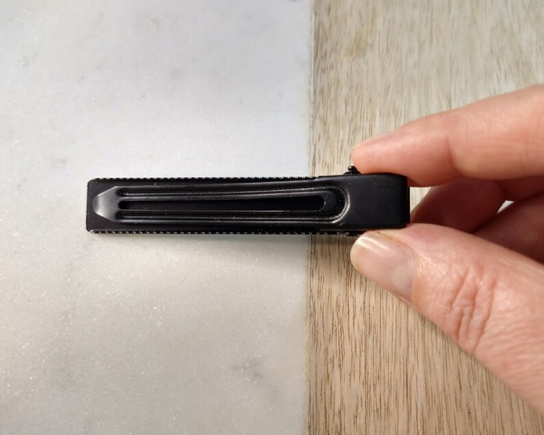 Peut inclure: Une pince &agrave; cheveux en m&eacute;tal noir avec une surface textur&eacute;e.