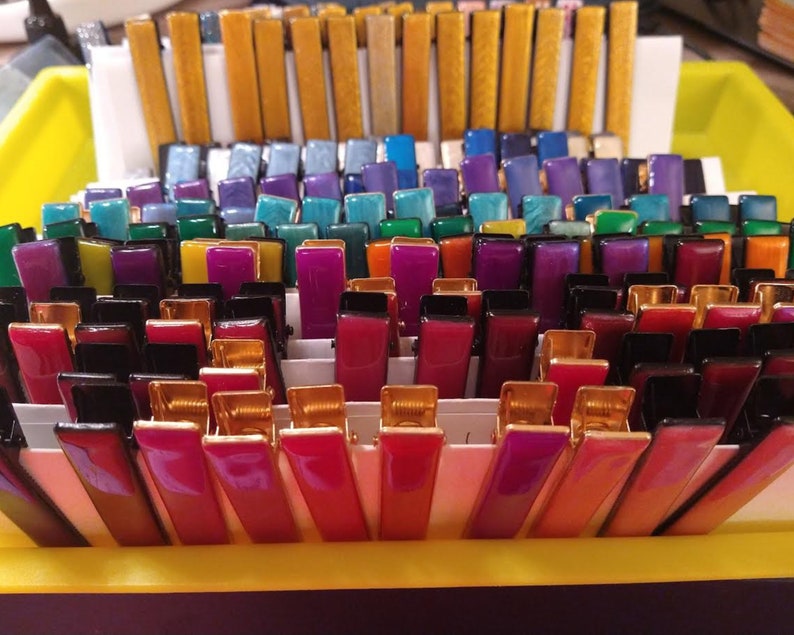 Peut inclure: Une collection de pinces &agrave; cheveux color&eacute;es dans une vari&eacute;t&eacute; de couleurs, notamment l'or, le bleu, le vert, le violet, le rouge et le noir. Les pinces sont dispos&eacute;es en rang&eacute;es et sont toutes de la m&ecirc;me taille et de la m&ecirc;me forme.