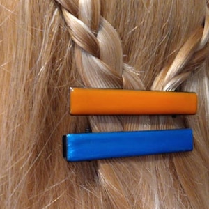 Peut inclure: Deux pinces &agrave; cheveux, l'une orange et l'autre bleue, sont fix&eacute;es dans une tresse de cheveux blonds.