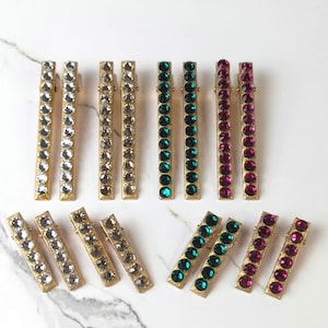 Puede incluir: Conjunto de diez pinzas para el pelo doradas con filas de diamantes de imitación. Las pinzas están disponibles en transparente, dorado, verde esmeralda y rojo rubí.