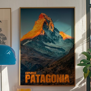 May include: A poster with a mountain range in the background and a large mountain peak in the foreground. The mountain peak is lit by the setting sun, giving it a warm orange glow. The text "EXPLORER PATAGONIA" is printed in orange at the bottom of the poster.
