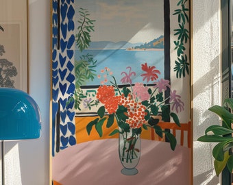 May include: A framed painting of a vase of flowers in front of a window with a view of a blue body of water and hills in the distance. The window has blue and white patterned curtains. The vase is clear glass and the flowers are red, pink, and purple.