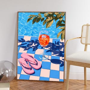 以下が含まれることがあります： 夏のシーンを描いた額入りのアートプリント。氷の入ったオレンジ色のカクテル、ピンクのビーチサンダル、青とピンクのチェック柄の表面が描かれています。背景にはプールと緑の葉が描かれています。