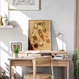 May include: A light wood desk with a gold lamp, a framed print of glasses of wine, and a potted plant. The desk has a drawer and a shelf. There are books on the shelf and a chair with a woven seat.
