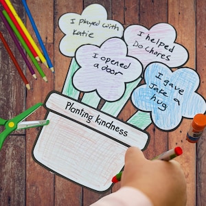 以下が含まれることがあります： 「優しさを植える」と書かれた植木鉢を使った、手描きのカラフルな工作プロジェクト。4つの花びらの形をした花には、「ケイティと遊んだ」や「ジェイクを抱きしめた」などのフレーズが表示されています。色鉛筆、ハサミ、スティックのりも散らばっています。