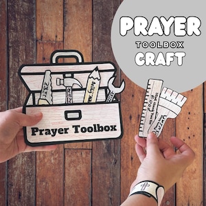 Op de afbeelding: Een papieren knutselset met een witte gereedschapskist met de tekst Prayer Toolbox, voorzien van illustraties van een zaag, hamer, potlood en moersleutel. Extra papieren uitsparingen bevatten een liniaal, een kwast met tekst en een polsbandje.