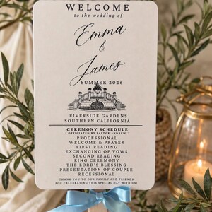 May include: A wedding program fan with a light blue ribbon. The program is cream-colored with elegant script announcing the wedding of Emma and James in Summer 2026. The ceremony schedule is also listed.