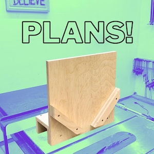 May include: A wooden woodworking jig with the word "PLANS!" in large black letters. The jig is made of light-colored plywood and is designed to be used with a table saw. The background is a light green color.