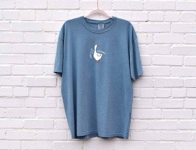 May include: A blue t-shirt with a white goose illustration and the text "Look at all the chickin'" printed on the front.