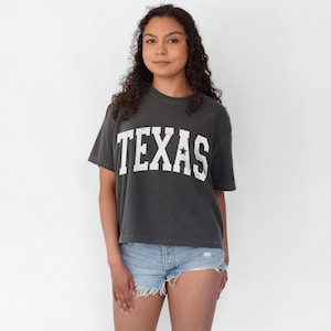 K&ouml;nnte beinhalten: Ein dunkelgraues, bauchfreies T-Shirt mit einem wei&szlig;en Vintage-Style "TEXAS"-Motiv und einem einzelnen wei&szlig;en Stern.