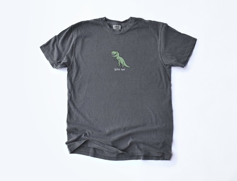 May include: A dark gray t-shirt with a green cartoon dinosaur and the text "bite me" printed on the front.