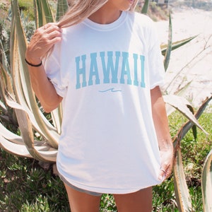 May include: White t-shirt with a light blue "HAWAII" graphic and a small wave design underneath.