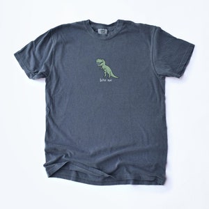 May include: A dark gray t-shirt with a green cartoon dinosaur and the text "bite me" printed on the front.