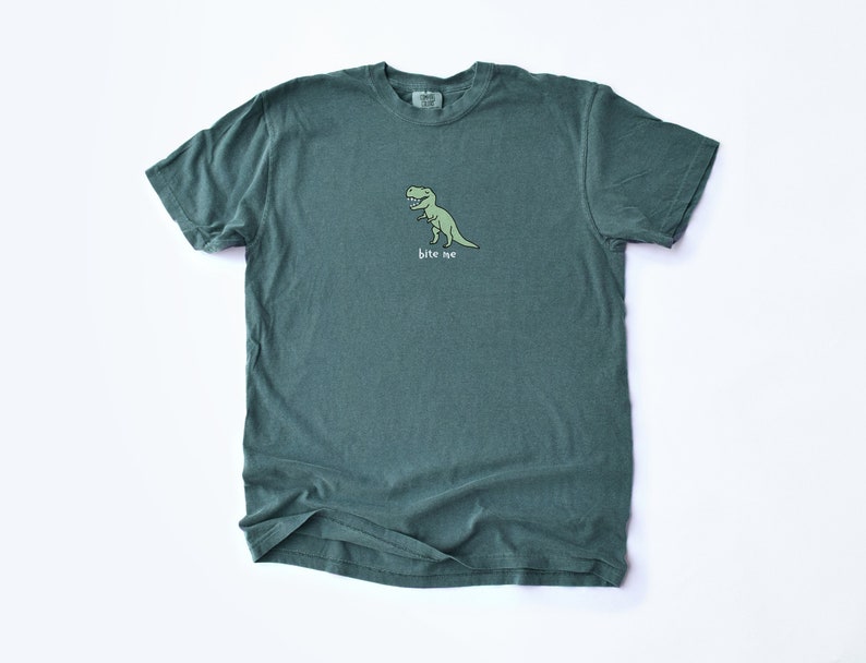 May include: A dark green t-shirt with a cartoon dinosaur graphic and the text "bite me" printed on the front.
