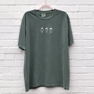 Op de afbeelding: Een donkergroen T-shirt met een wit geborduurd ontwerp van vier aardbeien.