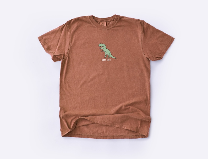 May include: A brown t-shirt with a green dinosaur graphic and the text "bite me".