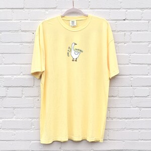 May include: A yellow short-sleeved t-shirt with a cartoon goose graphic and the text "Honk if you're a goose" printed on the front.