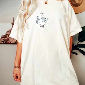 May include: A white oversized t-shirt with a cartoon goose graphic and the text "Look at all those chickens!"