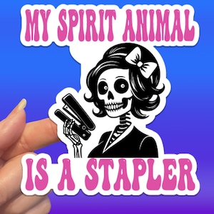 May include: A sticker with a skeleton illustration holding a stapler. The skeleton has black hair and a bow. The text "MY SPIRIT ANIMAL IS A STAPLER" is in pink bubble letters, set against a blue background.