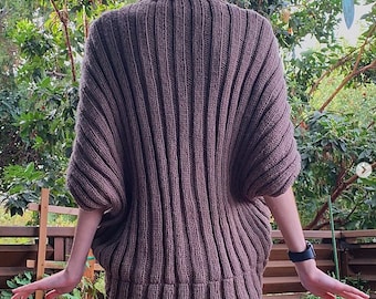 May include: A brown knitted sweater with a ribbed texture and a slightly oversized fit. The sweater has a high neckline and long sleeves.