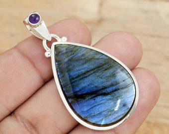 May include: A silver pendant featuring a teardrop-shaped labradorite gemstone with iridescent blue and green hues. The pendant has a small amethyst accent stone at the top.