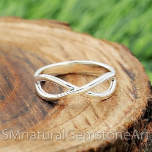 Könnte beinhalten: Ein silberner Unendlichkeitsring mit glatter, polierter Oberfläche. Der Ring wird auf einer Holzoberfläche präsentiert.
