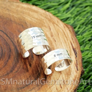 May include: Two silver hammered metal rings, one measuring 15 mm and the other 8 mm, are displayed on a wooden surface.