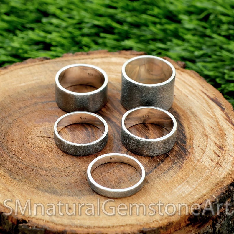 Op de afbeelding: Vijf zilveren ringen in verschillende maten, elk met een getextureerde afwerking, worden getoond op een houten oppervlak. De ringen zijn allemaal gestempeld met "925", wat aangeeft dat ze van sterling zilver zijn.