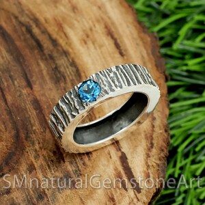 May include: A silver ring with a textured band and a blue gemstone set in the center.