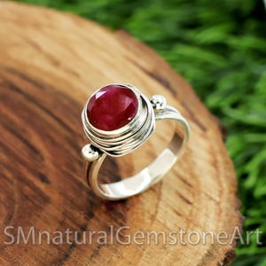 May include: A silver ring with a red ruby gemstone set in a wire-wrapped design.
