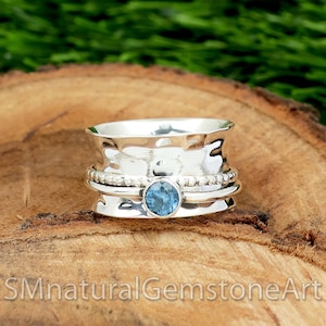 May include: A silver spinning ring with a blue gemstone in the centre. The ring has a hammered texture and is decorated with small beads.