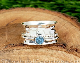 May include: A silver spinning ring with a blue gemstone in the centre. The ring has a hammered texture and is decorated with small beads.