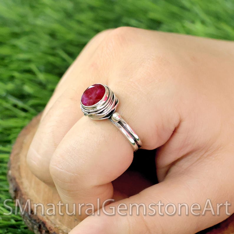 Puede incluir: Un anillo de plata con una piedra preciosa roja engastada en un dise&ntilde;o de alambre envuelto. El anillo est&aacute; en un dedo.