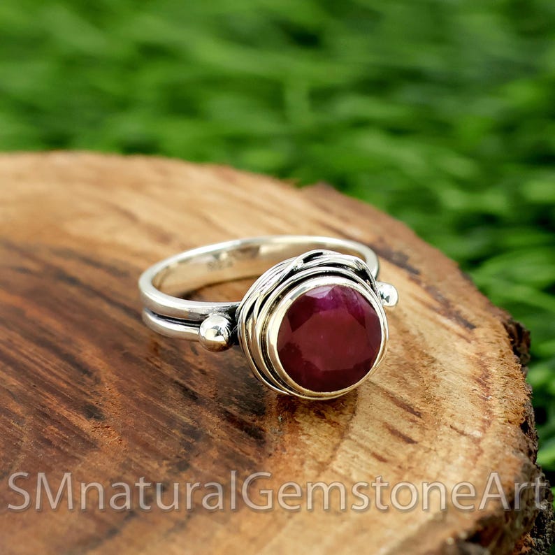 Puede incluir: Un anillo de plata con una piedra preciosa roja oscura engastada en un engaste envuelto en alambre. El anillo est&aacute; sobre una superficie de madera.