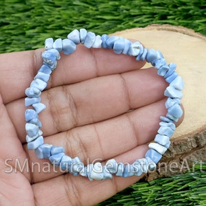 Puede incluir: Un brazalete de chips de piedra preciosa de color azul claro hecho con ópalo natural. El brazalete está hecho con pequeñas astillas de ópalo de forma irregular que están enhebradas en un cordón elástico transparente.