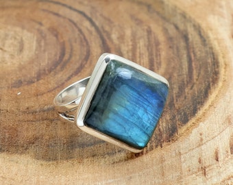 May include: A silver ring featuring a square-shaped blue labradorite gemstone. The ring has a simple, modern design.