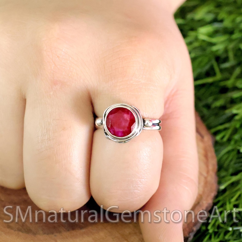 Puede incluir: Un anillo de plata con una piedra preciosa roja engastada en un engaste de bisel. El anillo est&aacute; en el dedo de una persona.