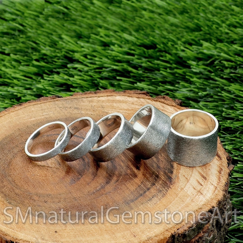 Op de afbeelding: Vijf zilveren ringen in verschillende maten, met een textuur, zijn gerangschikt in een aflopend patroon op een houten oppervlak. De ringen zijn allemaal van hetzelfde metaal en hebben een vergelijkbaar ontwerp.