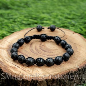 May include: Black lava rock beaded bracelet with a black cord and adjustable sliding knot closure. The bracelet is on a wooden surface.