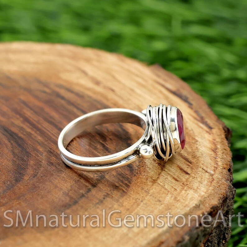 Puede incluir: Un anillo de plata con una piedra preciosa roja engastada en un dise&ntilde;o de jaula de alambre. El anillo est&aacute; sobre una superficie de madera.