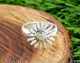 Könnte beinhalten: Ein silberner Ring mit einem Sonnenblumen-Design. Der Ring zeigt eine detaillierte Sonnenblume mit Blütenblättern und einem strukturierten Zentrum. Der Ring liegt auf einer Holzoberfläche mit dem Text "SMnaturalGemstoneArt" unten.