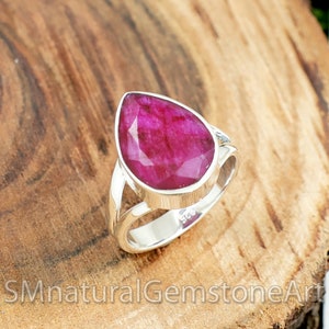 May include: A pear-shaped ruby gemstone set in a sterling silver ring with a split band design.